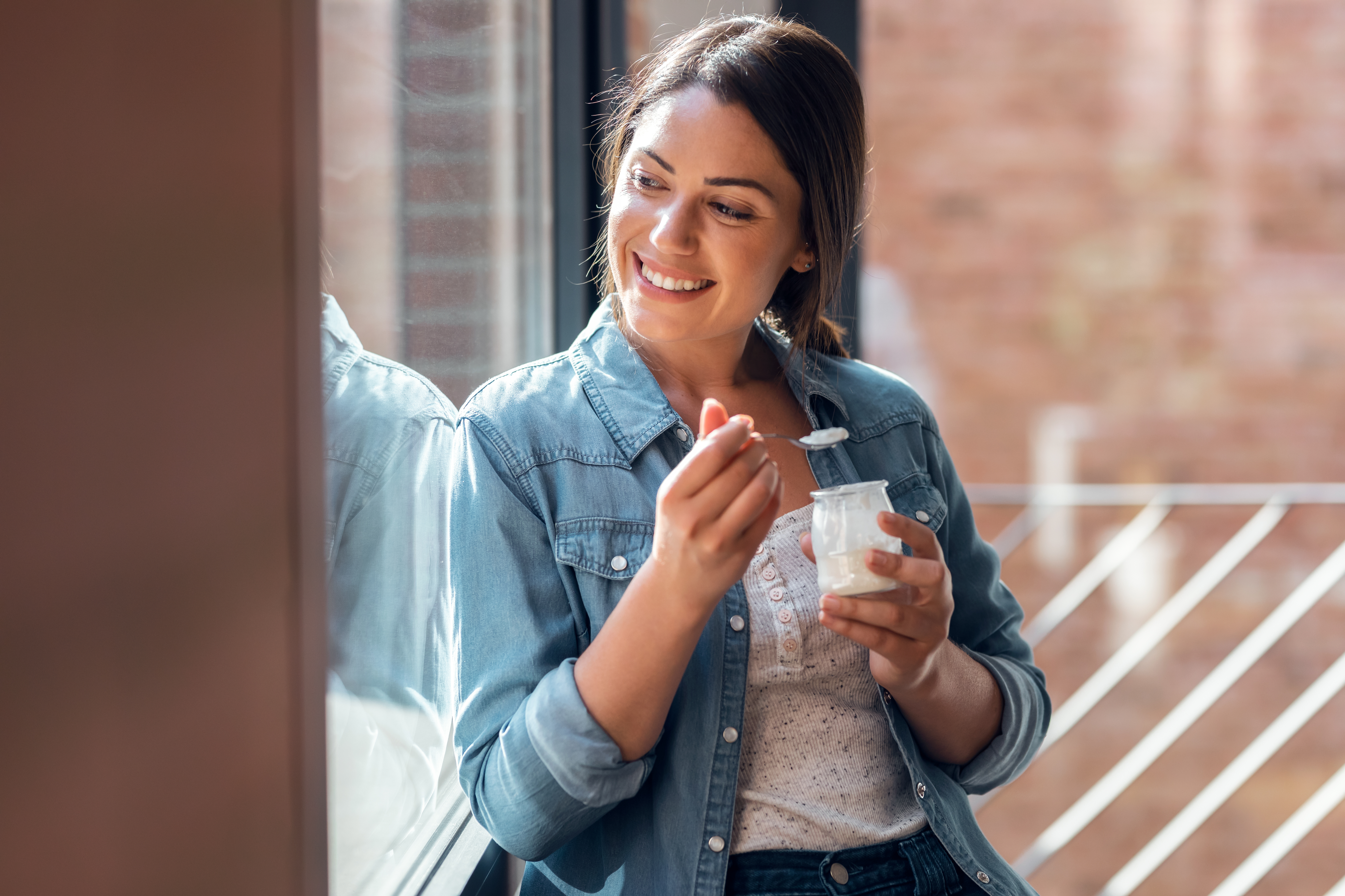 happy-beautiful-woman-eating-yogurt-while-standing-2024-09-22-08-20-35-utc.jpg